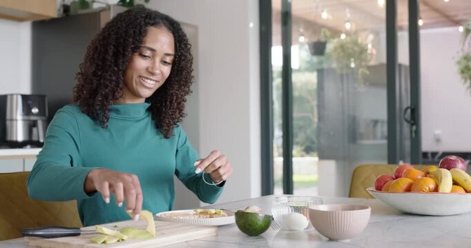 African American woman preparing meal at kitchen island, spreading topping, slicing pear with knife