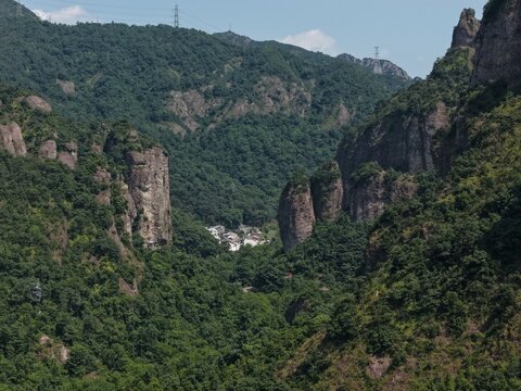 Aerial view of towering karst mountains in Lingfeng, Yandangshan, China, with a traditional temple nestled below. Dramatic limestone peaks and lush vegetation dominate the landscape.