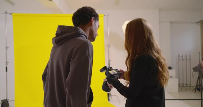 Photographer showing DSLR screen assistant viewing then adjusting softbox in studio yellow backdrop