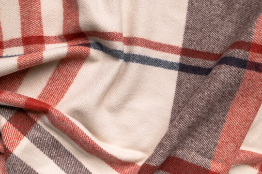 Classic plaid material lies in soft ripples, featuring warm red, cream and charcoal tones with detailed weave. Checkered fabric fits autumn styling, clothing production, textile education and layouts.