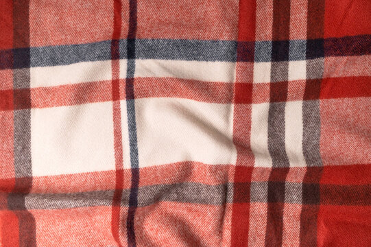 Classic plaid material lies in soft ripples, featuring warm red, cream and charcoal tones with detailed weave. Checkered fabric fits autumn styling, clothing production, textile education and layouts.