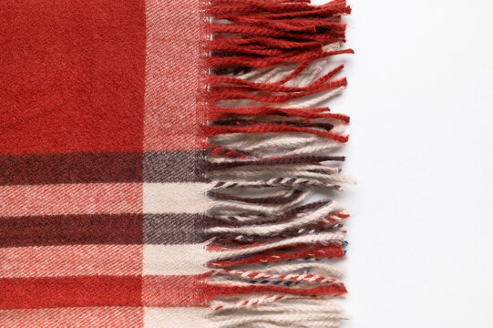 Autumn scarf in burgundy plaid lies folded on light gray background, with visible fringe and woven texture. Fashion marketing can present seasonal apparel, classic pattern, warmth and casual styling.