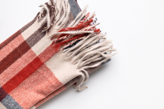 Autumn scarf in burgundy plaid lies folded on light gray background, with visible fringe and woven texture. Fashion marketing can present seasonal apparel, classic pattern, warmth and casual styling.