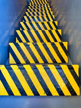 Close-up of yellow and black striped anti-slip steps on a metal staircase, highlighting industrial safety markings, improved visibility, slip prevention, and safe access in a working environment