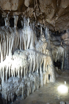 Detailed view of complex calcium carbonate draperies and stalactites covering a subterranean cave wall, with a bright spotlight highlighting the wet, dripping mineral textures.