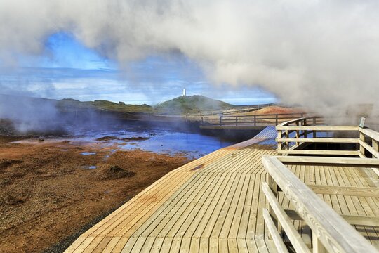 Wooden walkway in the high temperature area near Grindavik, behind it the lighthouse Reykjanesviti, peninsula Reykjanes, near Reykjavik, Iceland