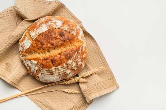 Round sourdough bread rests on linen beside wheat stalks, creating rustic bakery imagery. Warm texture supports artisan baking, food packaging, culinary education, and home cooking.