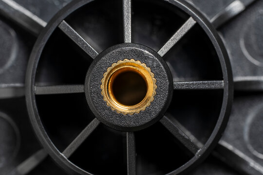 Black plastic wheel detail with brass metal threaded insert. Industrial plastic component with golden brass nut. Mechanical part with radial spokes for engineering, hardware and manufacturing concept