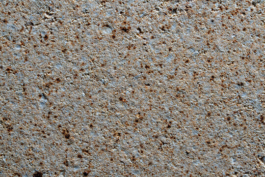 Rough stone wall texture with brown spots. Closeup of concrete or stucco surface with rusty speckles. Abstract gray concrete texture backdrop for industrial, construction and interior design