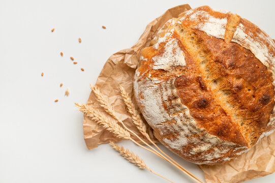 Round sourdough bread rests on linen beside wheat stalks, creating rustic bakery imagery. Warm texture supports artisan baking, food packaging, culinary education, and home cooking.