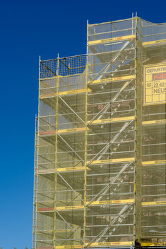 September 25, 2026, D&uuml;sseldorf, Germany - Building covered in scaffolding with yellow safety netting against a blue sky