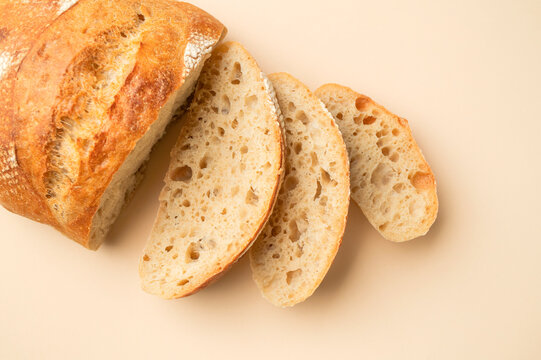 Fresh sourdough bread slices rest on beige background, showing crisp crust and airy crumb. Bakery marketing can use this rustic food image for artisan baking, freshness, quality and homemade appeal.