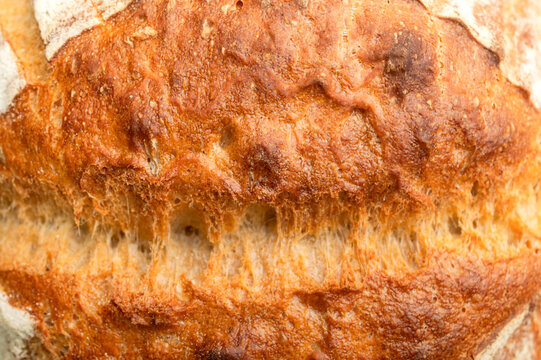 Close-up bread crust displays deep golden color, rough texture and toasted surface. Food advertising can feature sourdough baking, handcrafted quality, bakery products and appetizing visual texture.
