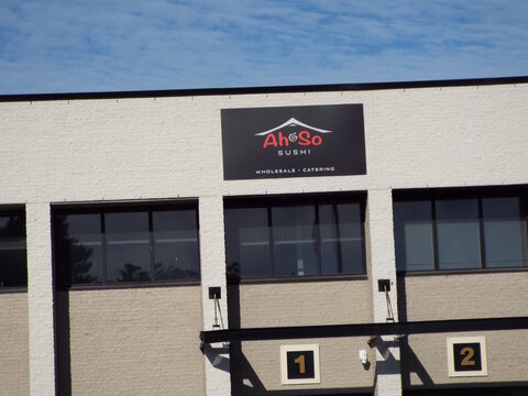 Gloucester, Ontario, Canada &ndash; August 1, 2026: A black and red sign for "Ah So Sushi Wholesale and Catering" is mounted on a white brick commercial building at 5459 Canotek Road Unit 1.
