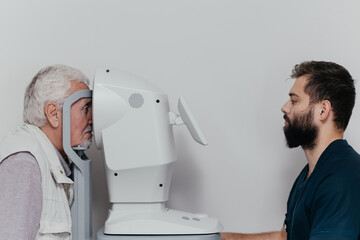 Mature male patient at dry eye analyzer during eye examination, doctor hand on joystick and eye image on screen. Ophthalmology clinic, vision test and eye care concept, copy space © Valeriia Stoganenko
