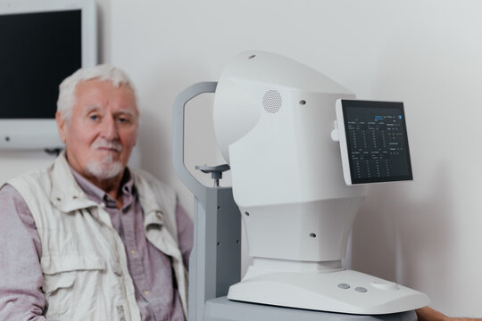 Modern ophthalmic biometer with IOL calculation results on screen, senior man patient in background in eye clinic. Cataract surgery planning, vision care and eye health concept