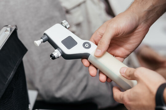 Doctor hands holding handheld rebound tonometer and disposable probe before eye pressure test, patient in background. Glaucoma screening and intraocular pressure measurement concept