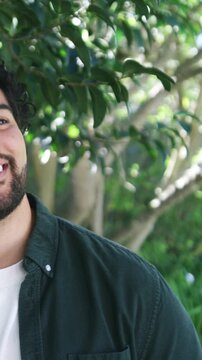 Vertical video: Smiling man wearing dark green shirt showing pocket laughing in yard, copy space