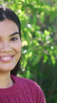 Vertical video: Smiling woman maroon cable-knit sweater hearing cue, turning in yard, sun flaring