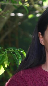 Vertical video: Panning cam showing woman right smiling at sun in garden, maroon knit, copy space