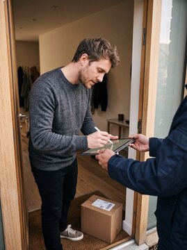 Young Man Signing Digital Tablet for Home Parcel Delivery Confirmation