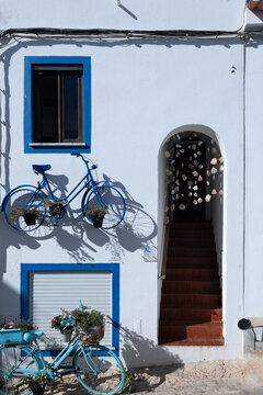 Whitewashed house facade with blue bicycle planters and seashell curtain in Burgau, Algarve, Portugal