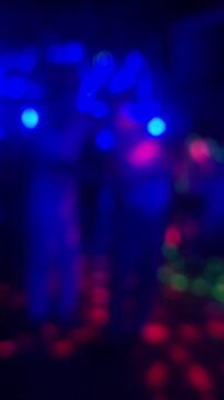 Defocused silhouette of couple dancing in night club during festive party event, handheld shot close up. Blurred bokeh laser light motion abstract background for music intro template.