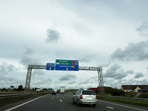 Highway traffic passes beneath overhead direction signs toward Vilnius, Riga, and Klaipėda in Lithuania