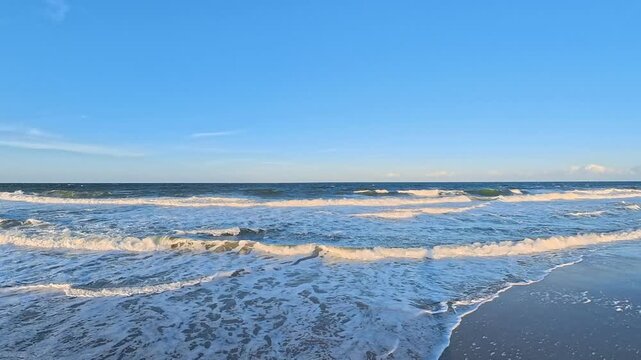 4K video shows sunlit breakers rolling toward a North Carolina sandy shore.