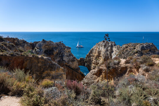Sailboat near natural rock arch and golden limestone cliffs at Ponta da Piedade, Algarve, Portugal