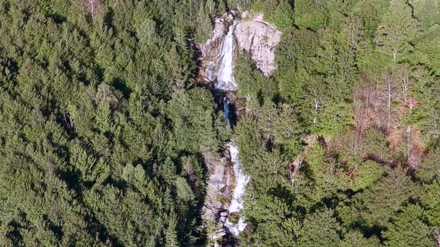 Aerial view of Cascada de Molieres waterfall cascading through alpine forest and granite mountain peaks, Val d'Aran, Pyrenees, Spain