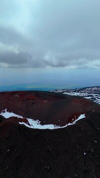 Drone aerial shot inside volcanic crater caldera on Mount Etna with snow patches in Sicily