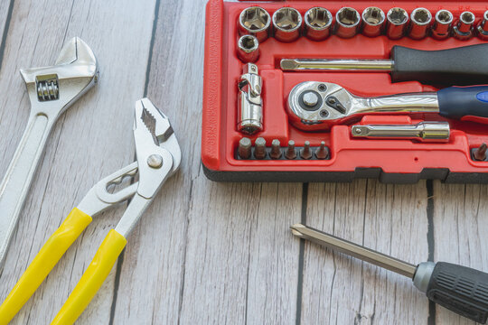A red socket wrench set box with pliers, adjustable wrench, and screwdriver on wood background with copy space.