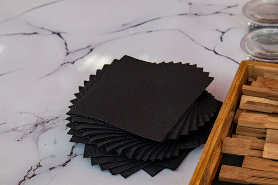 Fanned stack of black paper napkins on white marble background