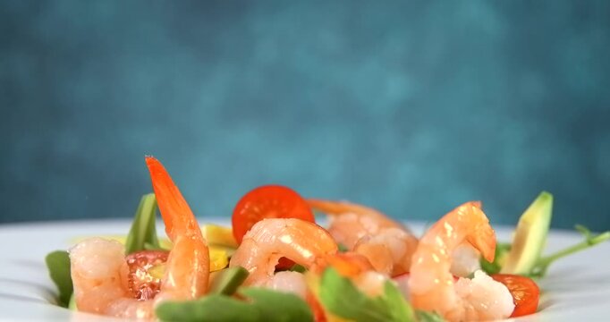 Shrimp falling onto fresh vegetable salad with avocado in slow motion