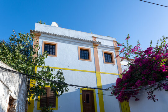 White house with yellow and orange trim and blooming bougainvillea under blue sky in Ferragudo, Algarve, Portugal