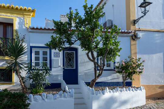 Whitewashed traditional house with blue door and citrus tree in a sunny village street, Ferragudo, Portugal