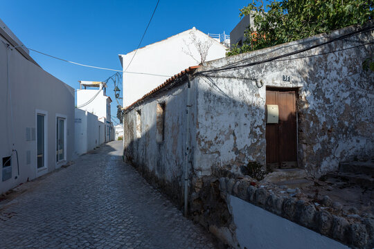 Narrow cobblestone street with old weathered house and whitewashed buildings in Ferragudo, Algarve, Portugal