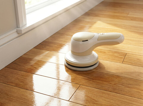 Modern cordless electric floor buffer and polisher machine cleaning and shining gleaming hardwood parquet flooring near a sunny white window frame in a bright contemporary residential living room
