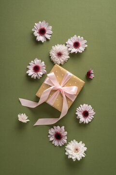 Pink ribbon gift box with daisy and chrysanthemum blooms on vertical green background for celebration