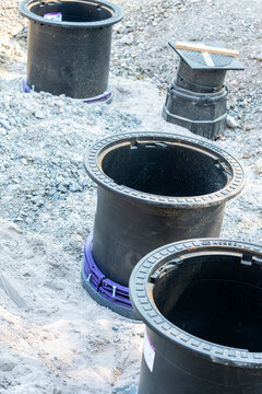 Multiple heavy-duty black plastic inspection shafts and drainage manholes are positioned in sand and crushed stone during the groundwork phase of a residential construction project.