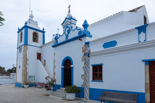 White and blue church with bell tower and cobblestone square in Alvor, Algarve, Portugal