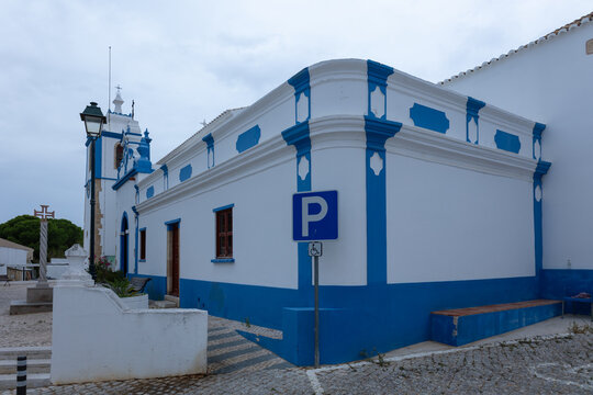 White and blue church exterior with parking sign on a cobblestone square in Alvor, Algarve, Portugal