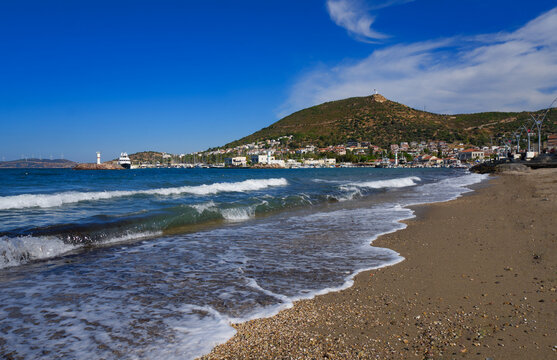 Beautiful sandy beach and sea waves with Yeni Foca resort town and mountains in the background, Izmir, Turkey.