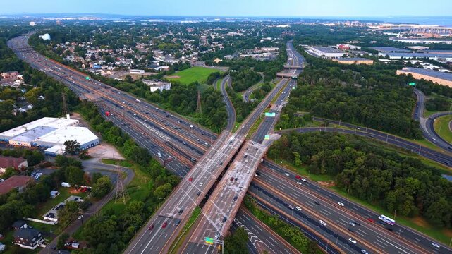 Large highway intersection surrounded by trees and a town. Two massive highways cross over each other, with one bridge stack going right over the road below it.