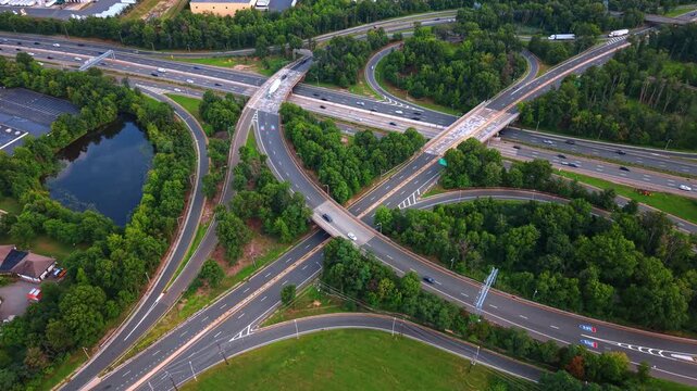 Modern complex highway interchange passing along beautiful green forest. Numerous vehicles run by the curved motorways in the suburbs.