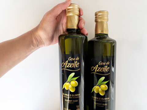 WARSAW, POLAND - MAY 1, 2026: Hand grasping the top of Casa de Azeite extra virgin olive oil bottle next to another bottle on white background. Concept of food retail, retail products, and packaging.
