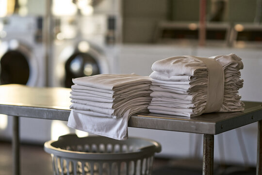 Folded white laundry in two stacks on a table near washing machines