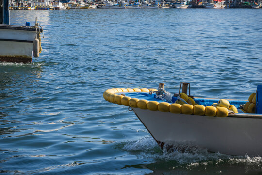 Small fishing boat equipped with yellow fenders sailing into calm harbor water for docking at traditional port in South Korea.