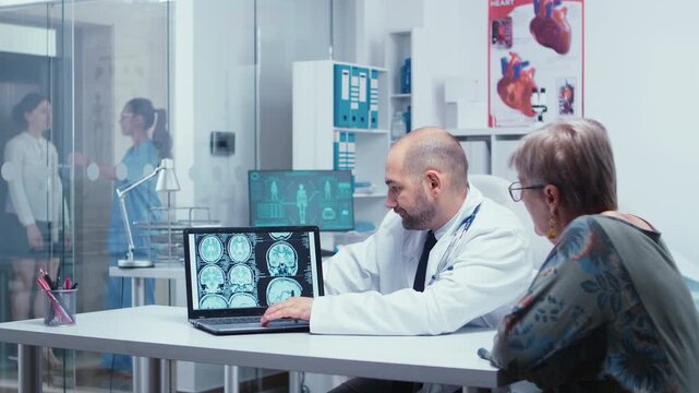 Doctor examines brain scan images on a laptop with an older woman during a clinic consultation, illustrating diagnostic imaging review, scan results, patient education and communication.